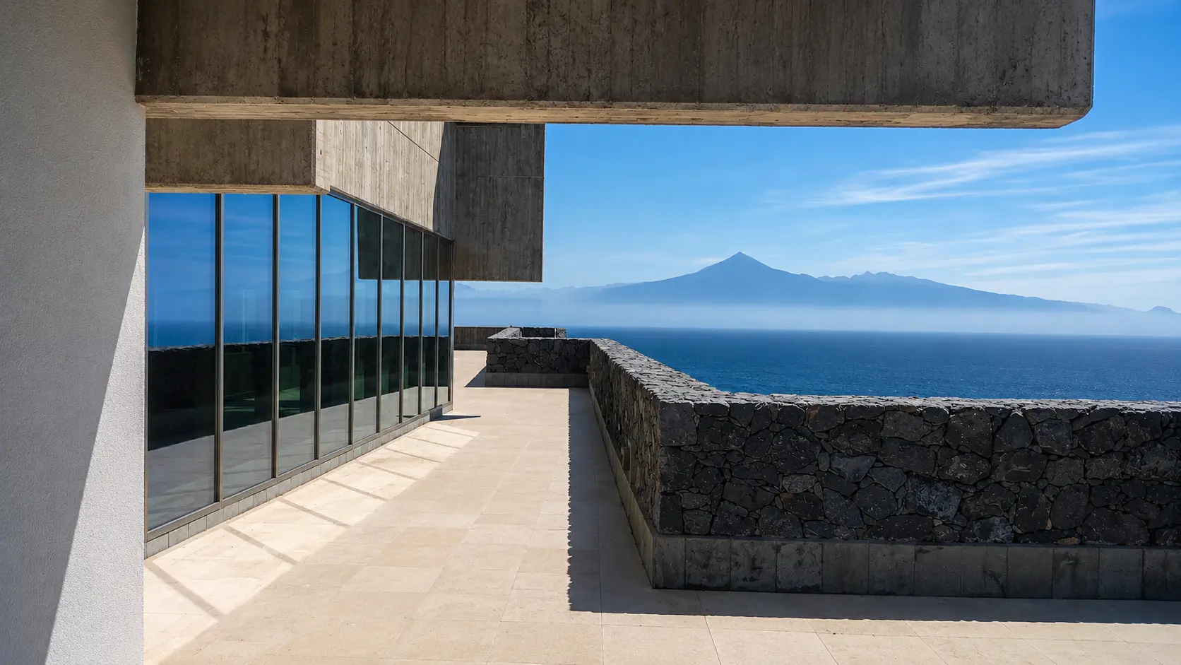 Terraza del hotel enmarcada por planos de hormigón y piedra con el océano y el Teide al fondo